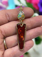 Gold pendant with amber and opal stones held in a hand against a neutral background